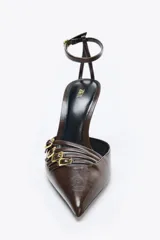 Zapato de tacón destalonado color marrón, con punta fina, tiras frontales con hebillas metálicas y pulsera al tobillo con cierre de hebilla.