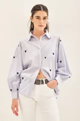 Camisa blanca de algodón con bordado de corazones dorados, corte amplio, cuello clásico, cartera con botones ocultos y bolsillo en el pecho.
