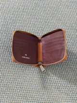 Billetera pequeña de cuero vacuno color bordó con cierre metálico y aplique de hongo. Interior con divisiones para tarjetas y forrería de tejido jacquard.