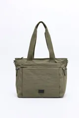 Cartera de nylon color verde militar con asas superiores reforzadas y correa larga regulable y desmontable. Cuenta con bolsillos frontales y laterales con cierre metálico, y un logo de la marca en la parte inferior central.