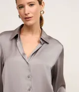 Camisa blanca de satén con cuello inglés, manga larga y cierre frontal con botones.