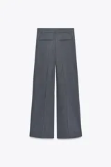 Pantalón marrón de tiro alto con trabillas, doble pliegue, bolsillos laterales y de vivo en la espalda, pernera ancha y cierre frontal con cremallera y gancho metálico.