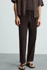 Pantalón de corte relajado (relaxed fit) color verde militar, confeccionado en mezcla de algodón y lino. Presenta cintura elástica ajustable con cordón y bolsillos frontales y traseros de vivo.