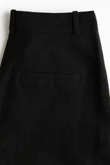 Pantalón negro de lino, de tiro alto, corte ancho y bolsillos laterales.
