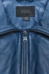 Cazadora azul de piel con cuello solapa, manga larga, bolsillos de vivo en delantero y cierre frontal con cremallera.