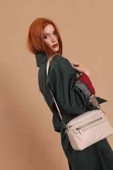 Bandolera color rosa viejo con detalles en cuero marrón claro, múltiples cremalleras metálicas y herrajes plateados. Incluye correa ancha ajustable con el logo de la marca.