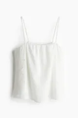 Top corto blanco de punto crepé con broderie, corte holgado, escote cuadrado y breteles finos ajustables.