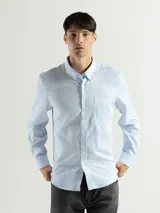 Camisa celeste y blanca a rayas verticales, de manga larga y corte clásico. Tiene cuello abotonado y bolsillo en el pecho.