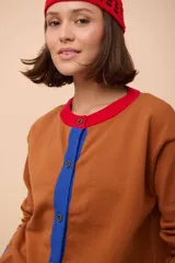 Cárdigan negro de punto con cuello redondo, cierre frontal con botones celestes y ribetes en cuello y puños de color rojo.