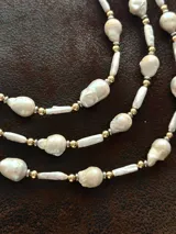 Collar corto de perlas de río alargadas y ovaladas, con cuentas de acero quirúrgico y bolitas con baño de oro. Cierre con cadena de acero quirúrgico y gancho para regular el largo.