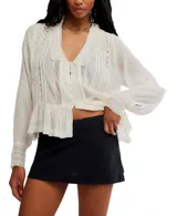 Blusa color crema de voile semitransparente con cuello y mangas largas con ribete de encaje, y botones en el frente.