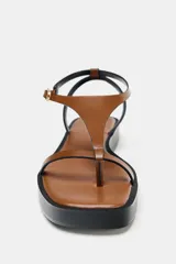 Sandalias planas color marrón con base negra, tira delantera fina y pulsera al tobillo con hebilla metálica dorada.