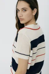 Remera polo tejida color crema con rayas horizontales en azul marino y rojo. Presenta cuello clásico, corte relajado y bordado de un ají rojo en el pecho.