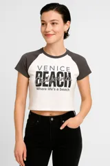 Remera corta blanca con mangas raglán grises y estampado frontal con texto 'Venice Beach California Where life's a beach'.