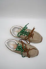 Zapatillas urbanas color marrón claro, confeccionadas en cuero, con cordones verdes y suela de goma.