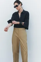 Pantalón color beige de corte ancho, con tiro medio, trabillas en la cintura y raya planchada.