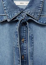 Camisa de jean celeste con cuello camisero y lazo al cuello, de manga larga con puños abotonados y corte recto.
