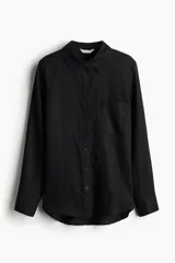 Camisa negra de lino liviano, con cuello clásico, cierre frontal con botones, canesú de doble capa en la espalda, hombros ligeramente caídos, mangas largas con puños abotonados, bolsillo de parche en el pecho y bajo redondeado.