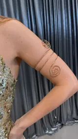 Brazalete dorado de metal con diseño de espiral en los extremos.