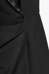 Mono corto negro con cuello smoking satinado, sin mangas y hombreras. Presenta detalle de frunce en la cintura y cierre cruzado con botones a presión.