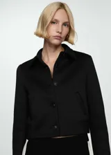 Chaqueta corta negra con cuello camisero, cierre frontal con botones, dos bolsillos laterales y forro interior.