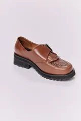 Zapato mocasín color marrón de cuero con hebilla metálica negra y detalle de flecos.