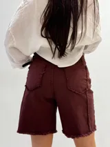 Bermuda marrón de gabardina elastizada con cinturón fino con tachas y detalles de flecos en el ruedo.