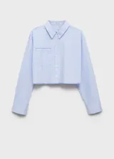 Camisa corta celeste a rayas verticales, de corte holgado, con cuello camisero, mangas largas con puños abotonados, bolsillo de parche en el pecho y cierre frontal con botones. Detalle de costuras a contratono.