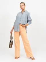 Pantalón de jean tiro alto color naranja claro, de corte ancho (wide leg) y bajo deshilachado. Presenta cinco bolsillos.