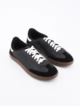 Zapatillas urbanas negras con cordones blancos y suela marrón.