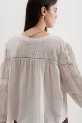 Camisa celeste de algodón con bordado calado, cuello en V y mangas largas abullonadas con puños elásticos.