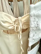 Minivestido de satén color crema, con breteles finos, escote con abertura y lazo ajustable, y corte a la cintura.