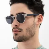 Lentes de sol INVU con montura redonda transparente y lentes polarizadas grises. Patillas finas de color gris oscuro.