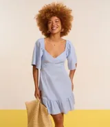 Vestido corto evasê de viscolino color crudo, con escote en V, mangas cortas amplias, recorte cut-out en los laterales de la cintura y volado en el ruedo.