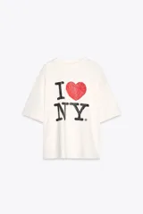 Remera color crudo de corte holgado con mangas cortas y cuello redondo. Estampado frontal con el texto "I ❤️ NY" en color negro y rojo.