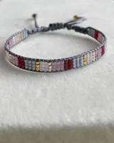 Pulsera tejida con cuentas Miyuki en tonos de gris, rosas, dorado, plateado y bordó. Es ajustable con cordón gris.