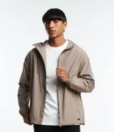 Campera rompevientos color beige con capucha ajustable con cordón, cierre frontal con cremallera, bolsillos laterales con cremallera y puños elásticos.