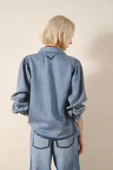 Camisa celeste de tencel, de calce recto, con manga larga amplia con frunces en los hombros y cuello camisero. Mangas terminadas en puño con botón y ojal. Cartera delantera con botones metálicos con el logo de la marca.