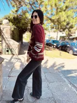 Sweater tejido color borgoña con diseño de copo de nieve en el frente y bordes con motivos geométricos en tonos beige, blanco y marrón.