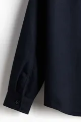 Sobrecamisa azul marino de tejido afieltrado con cuello, botones adelante y canesú en la espalda. Tiene bolsillos superiores con solapa, puños abotonados y bajo redondeado.