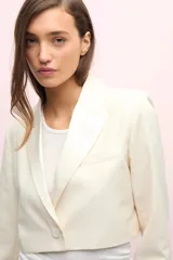 Blazer corto color blanco, de manga larga con solapa y bolsillo de pecho en tela brillosa.