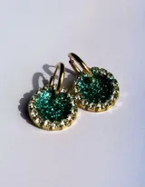 Par de aros colgantes con dije circular de resina con glitter multicolor y borde de strass. El arito es de acero quirúrgico dorado.