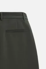 Pantalón relaxed fit color verde oscuro, con pliegues en la parte delantera, bolsillos laterales y traseros de ojal. Cierre frontal con cremallera y botón.