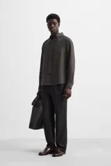 Camisa color arena de lino con cuello abotonado, manga larga con puños abotonados, corte regular y bajo con aberturas laterales.