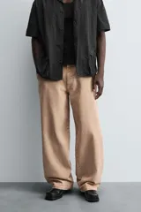 Pantalón de jean color beige, de corte ancho y tiro medio, con cinco bolsillos, efecto lavado y cierre frontal con cremallera y botón.
