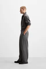 Pantalón negro de corte ancho con cinturón de tela con hebilla metálica y pliegues frontales.