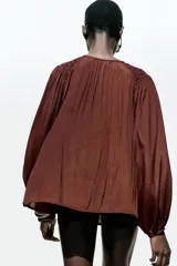 Blusa marrón con cuello redondo con cordón con abalorios, escote pico y manga larga abullonada. Cierre frontal con botones forrados a tono.