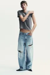 Camiseta gris de algodón con efecto lavado, cuello redondo y mangas cortas. Decoración con apliques de strass plateados en el escote.