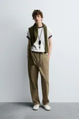 Pantalón color caqui de corte tapered relaxed fit, confeccionado en tejido de algodón. Presenta cintura con pliegues frontales dobles, bolsillos laterales en cadera y bolsillos traseros de vivo con botón. Cierre frontal con cremallera y botón.