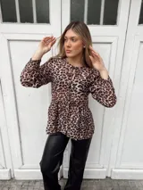Blusa marrón con estampado animal print, escote redondo con lazo ajustable, mangas largas con puños elásticos y corte peplum.